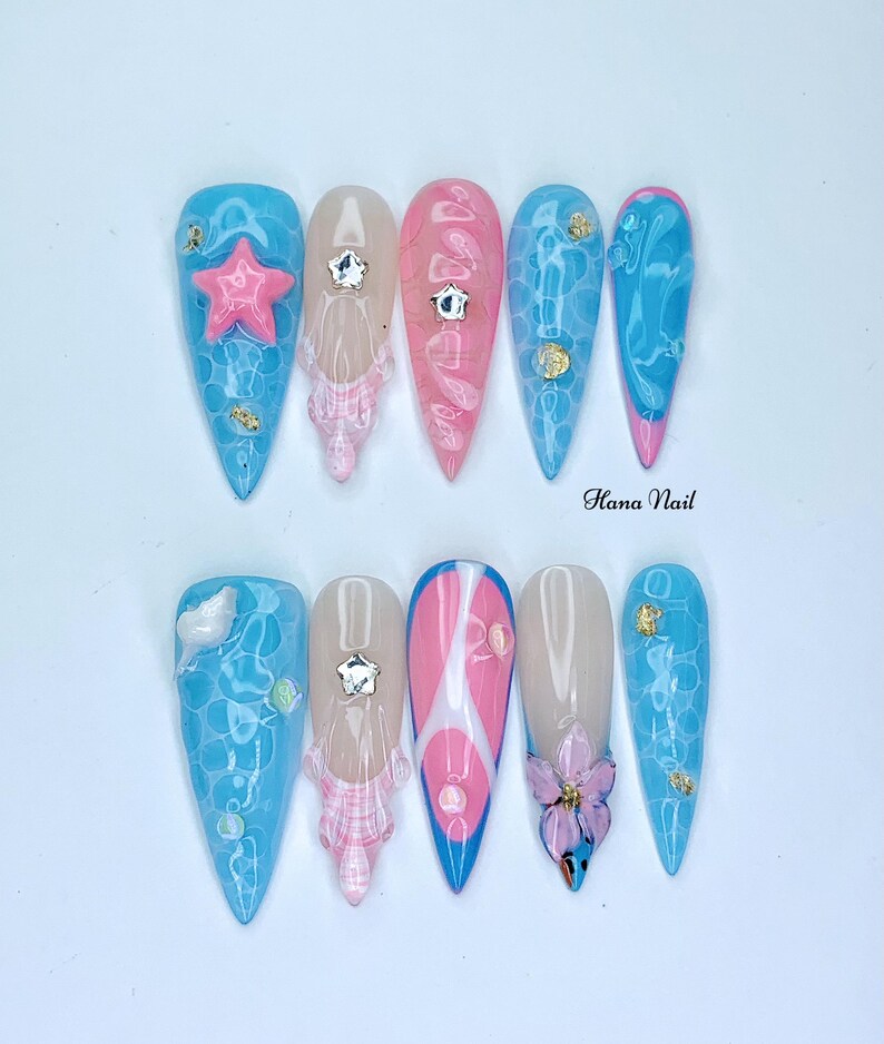 Puede incluir: Diez u&ntilde;as postizas largas y puntiagudas, azules y rosas, con varios dise&ntilde;os. Los dise&ntilde;os incluyen una flor rosa, una estrella de mar azul, un patr&oacute;n de cuadros blancos y rosas y un patr&oacute;n de remolino azul y blanco. Las u&ntilde;as est&aacute;n decoradas con diamantes de imitaci&oacute;n y purpurina dorada.
