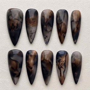 May include: A set of ten almond-shaped press-on nails featuring a glossy finish with a marbled, smoky pattern in shades of black, dark brown, and translucent beige. Each nail displays a unique, fluid ink-like design with varying dark gradients.