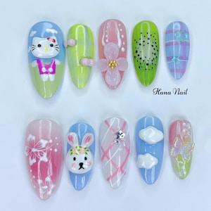 May include: A set of ten almond-shaped artificial nails with various designs. The designs include a Hello Kitty character, a kiwi fruit slice, a bunny, and floral and cloud motifs. The nails are painted in pastel colors like pink, blue, green, and yellow. The text "Hana Nail" is also visible.