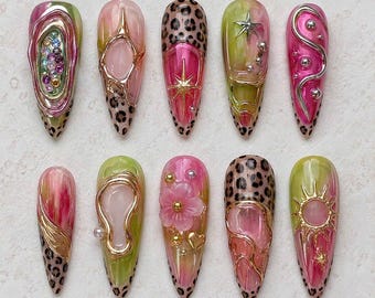 May include: A set of ten almond-shaped press-on nails featuring a mix of pink and lime green marbled bases, leopard print tips, and 3D metallic gold and silver accents including stars, flowers, hearts, and small rhinestones in various colors.