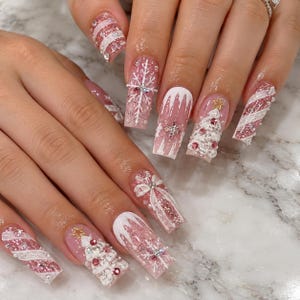 May include: Long square-shaped nails featuring a festive holiday theme with pink glitter, white accents, and 3D embellishments. Designs include white snowflakes, Christmas trees with gold stars, candy cane stripes, and bows adorned with rhinestones.