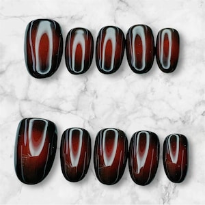 May include: Set of oval-shaped, press-on nails. Each nail features a gradient design, transitioning from a dark burgundy at the base to a lighter, almost white, color in the center. The nails are arranged in two rows on a marble surface.