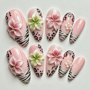 May include: A set of ten artificial nails in various designs. The nails feature a light pink base with 3D flower accents in pink and green. Some nails have leopard print or zebra stripes.