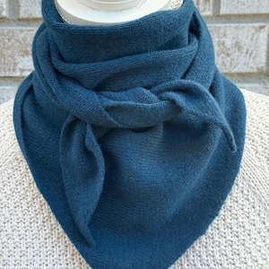 May include: A teal blue knitted scarf with a triangular shape. The scarf is folded and tied around a white mannequin's neck.