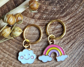 Può includere: Due marcapunti dorati con ciondoli. Un ciondolo è una nuvola bianca con un viso sorridente. L'altro ciondolo è un arcobaleno con strisce rosa, gialle e viola.