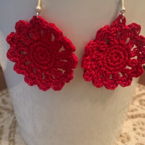 May include: A pair of red crocheted earrings with silver hooks. The earrings are round and have a flower-like design.