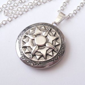 May include: A silver-colored compass pendant necklace. The round pendant features a detailed compass rose design with a central sunburst and floral border. The necklace has a delicate chain.