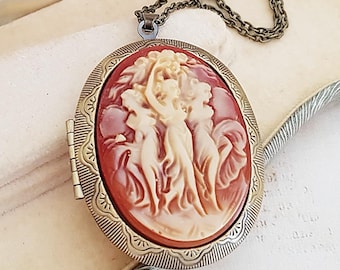 May include: A vintage-style cameo locket necklace with a red and white cameo featuring three women. The locket is made of brass and has a chain.