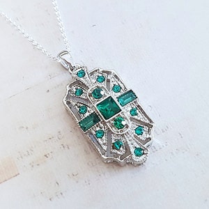 May include: A silver necklace with a green crystal pendant. The pendant is a geometric design with a filigree pattern.