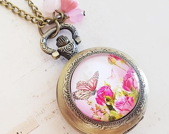 May include: A gold-toned pocket watch necklace with a pink butterfly and floral design on the face. The necklace has a chain and pink glass beads.