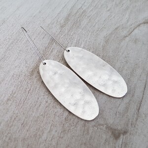 May include: A pair of silver oval earrings with a hammered texture and thin silver hooks.