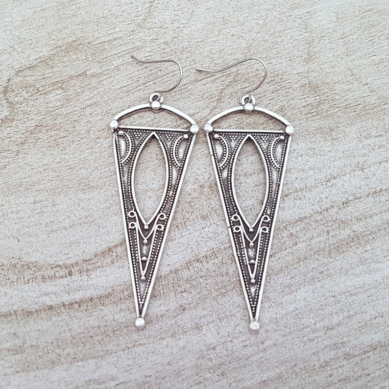 May include: A pair of silver dangle earrings with a geometric, triangular design. The earrings have a detailed, intricate pattern.