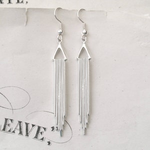 May include: Silver dangle earrings with a triangle design and a long, thin, vertical chain of connected bars.