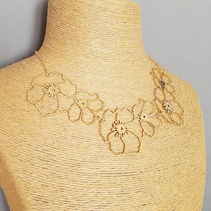 May include: A gold-colored floral necklace displayed on a mannequin. The necklace features five openwork flower pendants connected by a delicate chain. The flowers have detailed centers and petal outlines, creating an elegant and artistic design.