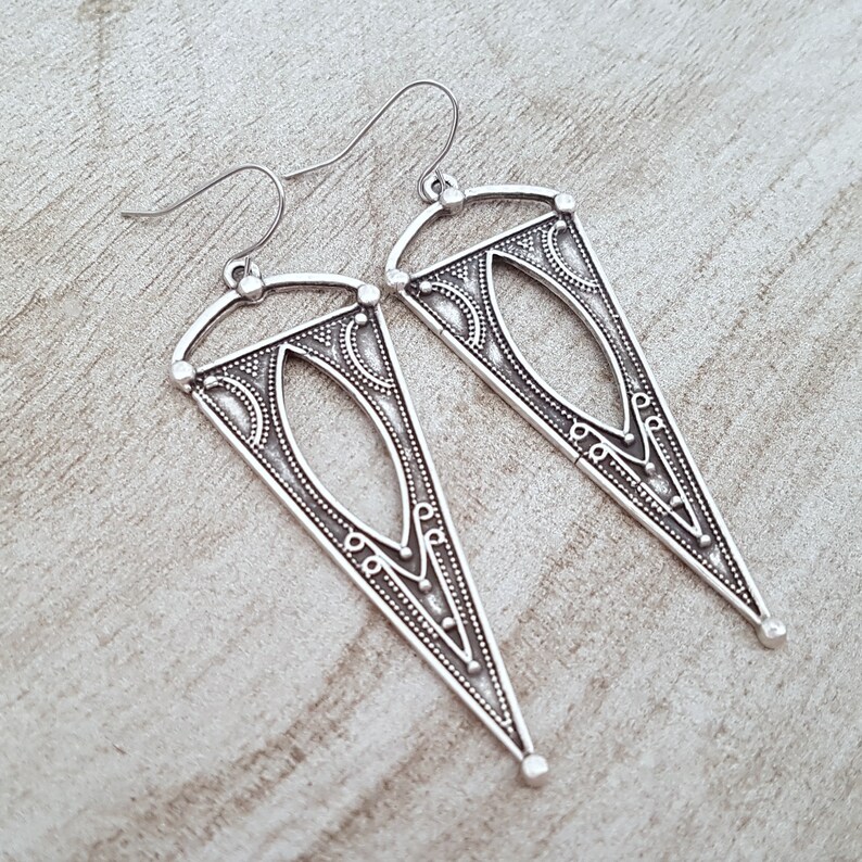 May include: A pair of silver dangle earrings with a geometric triangle design. The earrings have a detailed pattern and a silver hook closure.
