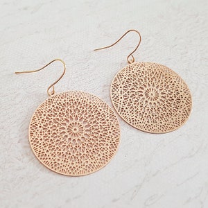 Può includere: Un paio di orecchini dorati con un design circolare che presenta un motivo delicato e intricato. Gli orecchini hanno una semplice chiusura a gancio.