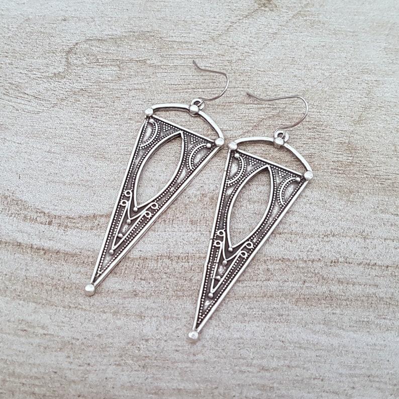 May include: A pair of silver triangle-shaped earrings with intricate geometric designs.