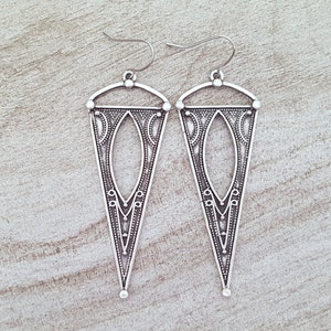 May include: A pair of silver triangle earrings with intricate geometric designs. The earrings have a hook closure.