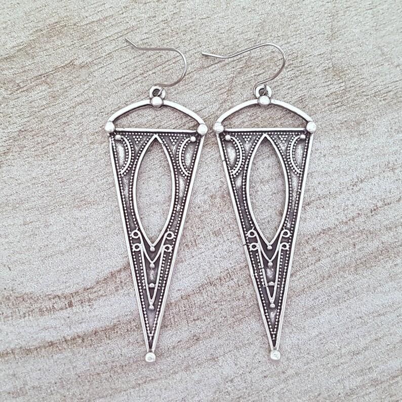 May include: A pair of silver triangle earrings with intricate geometric designs. The earrings have a hook closure.