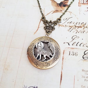 May include: A gold tone necklace with a locket featuring a silver wolf howling at the moon. The locket is surrounded by an intricate floral design.