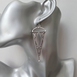 May include: Silver dangle earrings with a geometric triangle design. The earrings have a detailed, intricate pattern.