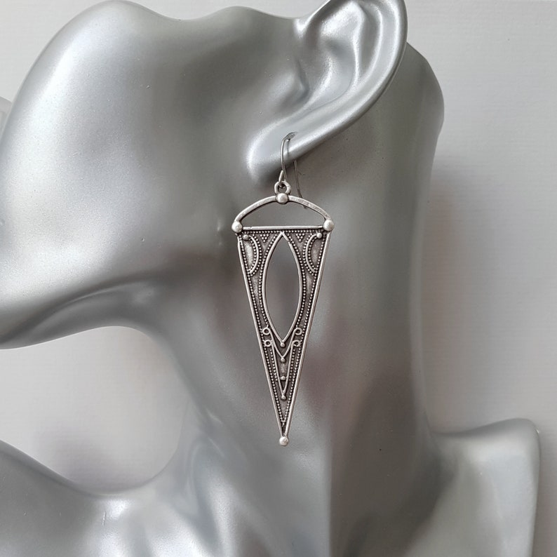 May include: Silver dangle earrings with a geometric triangle design. The earrings have a detailed, intricate pattern.