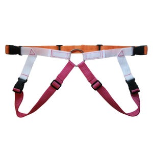 May include: A dog harness with an orange neck strap and pink and white body straps. The harness has black plastic buckles and a metal ring for leash attachment. The straps are adjustable for a comfortable fit.