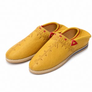 May include: A pair of yellow leather slippers with decorative stitching and red and blue accents. The slippers have a rounded toe and a low profile, with a beige sole. The design includes a geometric pattern.