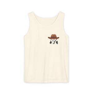 May include: Cream-colored tank top with a small graphic of a cowboy hat and the number 7. The cowboy hat is brown with the initials "AD" on the front. The number 7 is black and white.