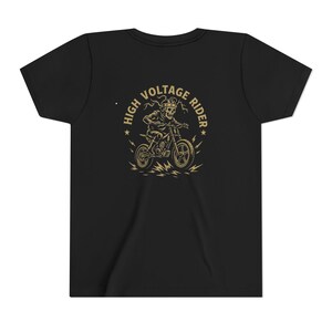 Puede incluir: Camiseta negra con un diseño dorado de un esqueleto montando una moto. El diseño incluye el texto "HIGH VOLTAGE RIDER" y rayos. La camiseta está hecha de un material suave y cómodo.