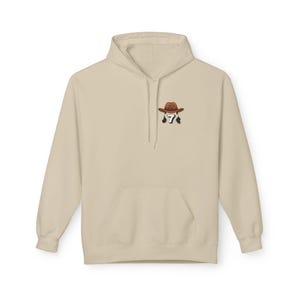 May include: A beige hoodie with a kangaroo pocket and a drawstring hood. The hoodie features a small embroidered design of a cowboy hat and the number 7 on the upper left chest.