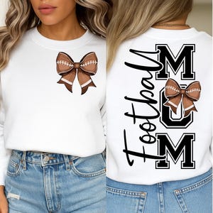 May include: White sweatshirt featuring a brown football-shaped bow on the front. The back of the sweatshirt displays the text "Football Mum" in black script and block letters, with a football bow graphic.
