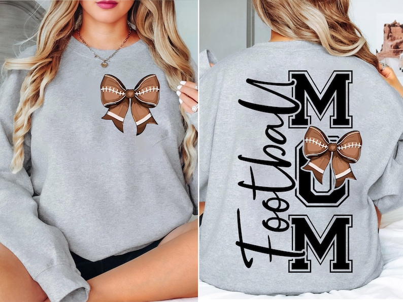 May include: A light gray sweatshirt featuring a brown football-shaped bow. The back of the sweatshirt displays the words "Football Mum" in black. The bow design is repeated on the back, above the word "MUM".