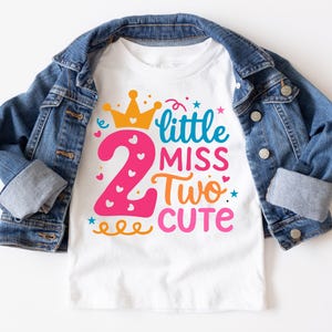May include: White t-shirt with a pink number 2, a gold crown, and the text "little miss two cute" in colorful letters.