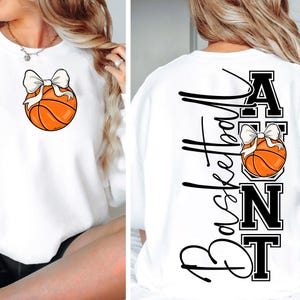 Op de afbeelding: Witte sweatshirt met een basketbalafbeelding en een witte strik. De achterkant van de sweatshirt heeft het woord "Basketball" in een verticaal script, samen met het woord "ANT" en een andere basketbalafbeelding.
