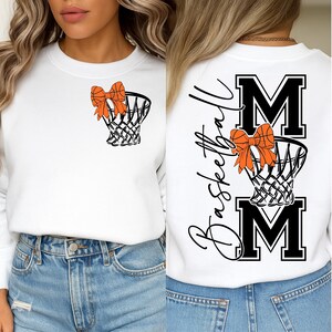 Puede incluir: Sudadera blanca con un dise&ntilde;o de red de baloncesto y lazo naranja. La parte trasera muestra la palabra "Basketball" en cursiva, con "MOM" en letras negritas, y otra red de baloncesto con un lazo naranja.