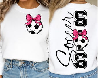 May include: White sweatshirt featuring a soccer ball with a pink bow. The front of the sweatshirt has the soccer ball graphic, while the back displays the word "Soccer" in a script font with the soccer ball graphic and the letter "S".