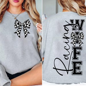Puede incluir: Una sudadera gris claro con un lazo a cuadros blanco y negro en la parte delantera. La parte trasera de la sudadera muestra las palabras "Racing Wife" en un diseño vertical, con un lazo a cuadros y letras en bloque.