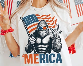Peut inclure: T-shirt blanc avec un motif d'une créature ressemblant à Bigfoot portant des lunettes de soleil et tenant un drapeau américain. Le mot "'MERICA" est imprimé en orange et bleu. Le design est patriotique et adapté au jour de l'Indépendance.