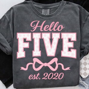 Puede incluir: Camiseta gris oscuro con el texto "Hello FIVE" en rosa en cursiva y letras de bloque. La palabra "FIVE" tiene un estampado floral. Un lazo rosa y el texto "est. 2020" están debajo.