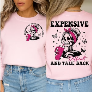 May include: Light pink sweatshirt with a graphic of a skeleton wearing a pink headband and holding a pink tumbler. The text on the front says "Expensive Difficult and Talk Back". The back of the sweatshirt has the same graphic and the text "Expensive Difficult and Talk Back".