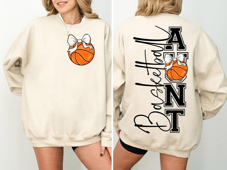 Op de afbeelding: Cr&egrave;mekleurige sweatshirt met een basketbal en een witte strik. De achterkant toont het woord "Basketball" in script, met "AUNT" in blokletters, en een andere basketbal met een strik.