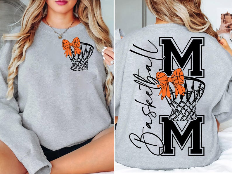 Puede incluir: Sudadera gris claro con una red de baloncesto y un lazo naranja. La parte trasera de la sudadera tiene la palabra "Basketball" en cursiva, con las letras "MOM" en negrita, en negro.