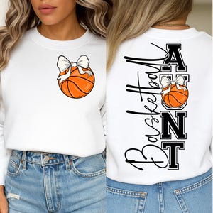Op de afbeelding: Witte sweatshirt met een basketbal en een witte strik op de voorkant. De achterkant toont het woord "Basketball" in cursief, met "AUNT" in blokletters en een basketbalafbeelding.