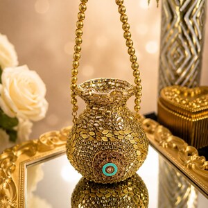 May include: A gold-toned pot-shaped handbag featuring an intricate exterior of small square mirrors and metallic leaf-shaped embellishments. The bag has a beaded handle and a central circular accent with a bright turquoise blue enamel inlay.