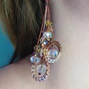 May include: A pair of long, brown and beige beaded earrings with crystal accents. The earrings feature a tassel design with multiple strands of beads and a circle of beads at the bottom.
