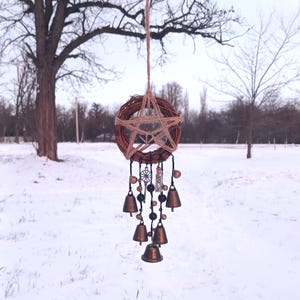 Peut inclure: Un attrape-rêves artisanal avec une couronne tressée marron et une étoile en jute au centre. Des cloches et des perles en bronze pendent en dessous. L'attrape-rêves est suspendu par une ficelle de jute, sur un fond enneigé.