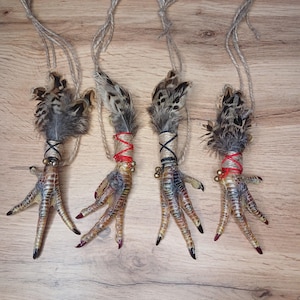 Op de afbeelding: Vier decoratieve vogelpootornamenten met veren, touw en kleine belletjes. De poten zijn beschilderd met een kleurengradi&euml;nt en de tenen zijn rood en zwart geschilderd. Elk ornament wordt opgehangen met een stuk touw.