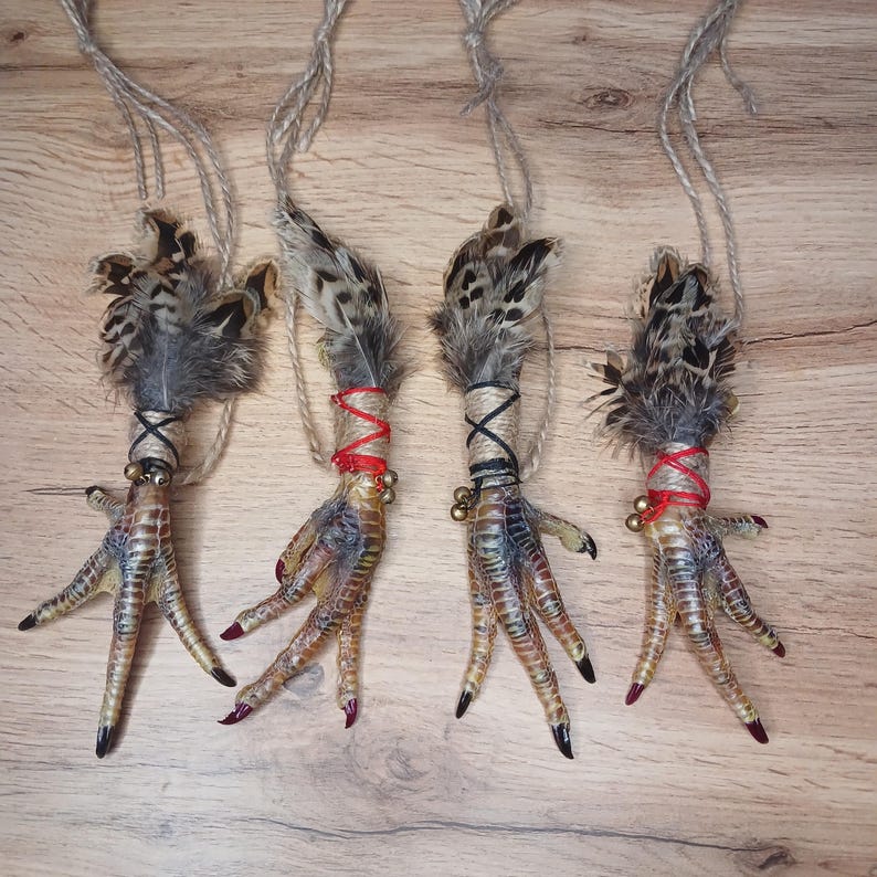 Op de afbeelding: Vier decoratieve vogelpootornamenten met veren, touw en kleine belletjes. De poten zijn beschilderd met een kleurengradi&euml;nt en de tenen zijn rood en zwart geschilderd. Elk ornament wordt opgehangen met een stuk touw.