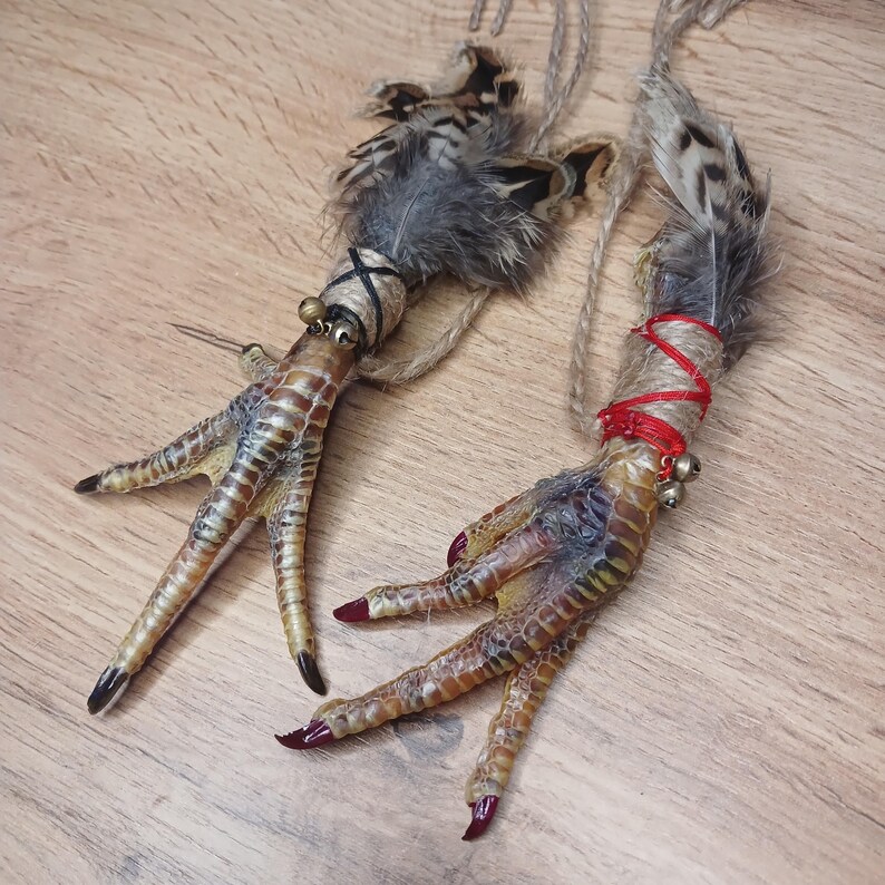 Op de afbeelding: Twee decoratieve vogelpoten met veren en touw. E&eacute;n voet is omwikkeld met zwart touw en heeft een klein belletje. De andere voet is omwikkeld met rood touw en heeft twee kleine belletjes. De teennagels zijn donkerrood geverfd.